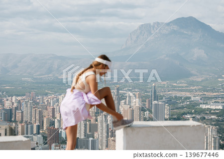 Female hiker overlooks urban cityscape with mountains in background Female hiker overlooks urban cityscape with mountains in background 139677446