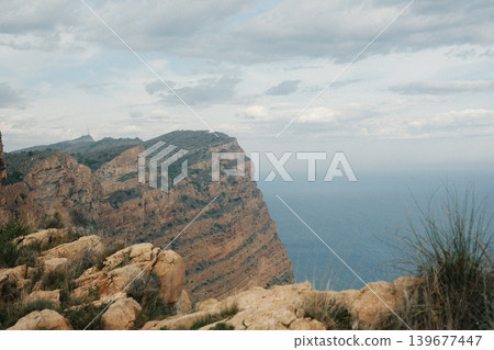 Majestic coastal cliff view overlooking the blue ocean and cloudy sky Majestic coastal cliff view overlooking the blue ocean and cloudy sky 139677447