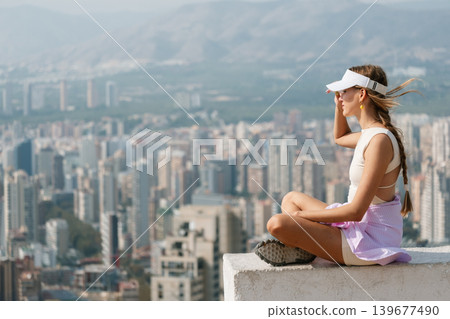 Woman in visor enjoys scenic cityscape view from rooftop Woman in visor enjoys scenic cityscape view from rooftop 139677490