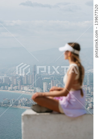 Woman relaxing on cliff edge with scenic cityscape and coastline view Woman relaxing on cliff edge with scenic cityscape and coastline view 139677520