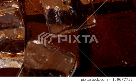 Cola with Ice. Close up of the ice cubes in cola water. Texture of carbonate drink with bubbles in glass. Cola soda and ice splashing fizzing or floating up to top of surface. Cold drink background. Cola with Ice. Close up of the ice cubes in cola water. Texture of carbonate drink with bubbles in glass. Cola soda and ice splashing fizzing or floating up to top of surface. Cold drink background. 139677732