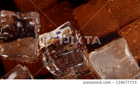Cola with Ice. Close up of the ice cubes in cola water. Texture of carbonate drink with bubbles in glass. Cola soda and ice splashing fizzing or floating up to top of surface. Cold drink background. Cola with Ice. Close up of the ice cubes in cola water. Texture of carbonate drink with bubbles in glass. Cola soda and ice splashing fizzing or floating up to top of surface. Cold drink background. 139677733