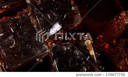 Cola with Ice. Close up of the ice cubes in cola water. Texture of carbonate drink with bubbles in glass. Cola soda and ice splashing fizzing or floating up to top of surface. Cold drink background. Cola with Ice. Close up of the ice cubes in cola water. Texture of carbonate drink with bubbles in glass. Cola soda and ice splashing fizzing or floating up to top of surface. Cold drink background. 139677736
