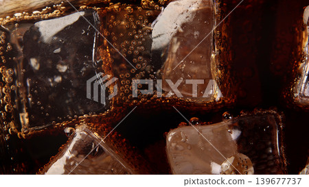 Cola with Ice. Close up of the ice cubes in cola water. Texture of carbonate drink with bubbles in glass. Cola soda and ice splashing fizzing or floating up to top of surface. Cold drink background. Cola with Ice. Close up of the ice cubes in cola water. Texture of carbonate drink with bubbles in glass. Cola soda and ice splashing fizzing or floating up to top of surface. Cold drink background. 139677737