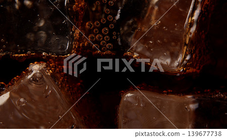 Cola with Ice. Close up of the ice cubes in cola water. Texture of carbonate drink with bubbles in glass. Cola soda and ice splashing fizzing or floating up to top of surface. Cold drink background. Cola with Ice. Close up of the ice cubes in cola water. Texture of carbonate drink with bubbles in glass. Cola soda and ice splashing fizzing or floating up to top of surface. Cold drink background. 139677738