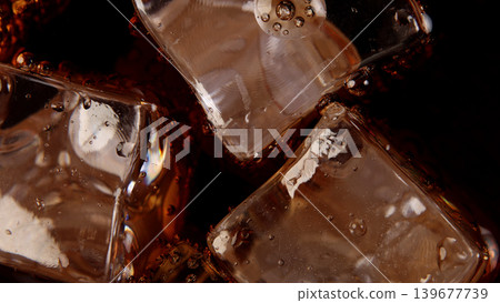 Cola with Ice. Close up of the ice cubes in cola water. Texture of carbonate drink with bubbles in glass. Cola soda and ice splashing fizzing or floating up to top of surface. Cold drink background. Cola with Ice. Close up of the ice cubes in cola water. Texture of carbonate drink with bubbles in glass. Cola soda and ice splashing fizzing or floating up to top of surface. Cold drink background. 139677739