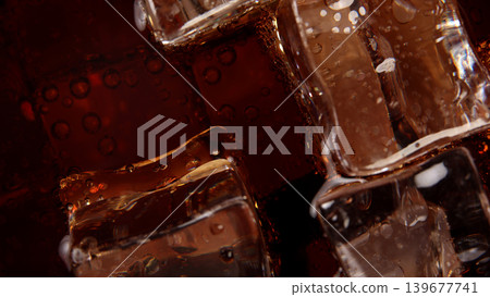 Cola with Ice. Close up of the ice cubes in cola water. Texture of carbonate drink with bubbles in glass. Cola soda and ice splashing fizzing or floating up to top of surface. Cold drink background. Cola with Ice. Close up of the ice cubes in cola water. Texture of carbonate drink with bubbles in glass. Cola soda and ice splashing fizzing or floating up to top of surface. Cold drink background. 139677741