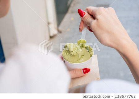 Woman enjoying matcha ice cream with red nails on a sunny day outdoors Woman enjoying matcha ice cream with red nails on a sunny day outdoors 139677762
