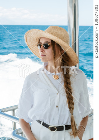 Stylish woman in sun hat and sunglasses relaxing on a boat at sea Stylish woman in sun hat and sunglasses relaxing on a boat at sea 139677803