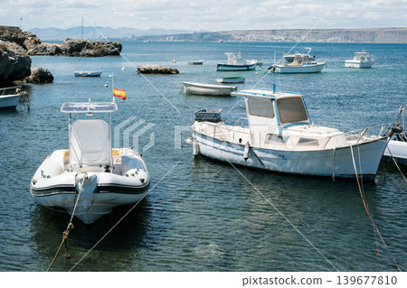 Serene coastal harbor with moored boats under cloudy sky in mediterranean landscape Serene coastal harbor with moored boats under cloudy sky in mediterranean landscape 139677810