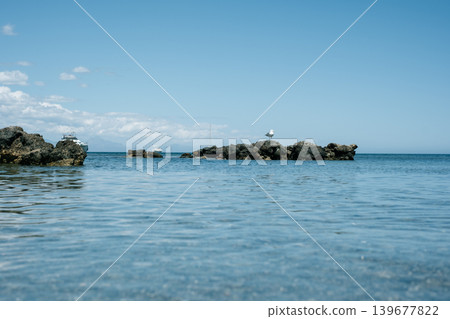 Serene rocky shoreline overlooking calm ocean with blue sky horizon Serene rocky shoreline overlooking calm ocean with blue sky horizon 139677822