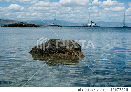 Tranquil coastal view with sailboats and rocky shore under cloudy sky 139677826