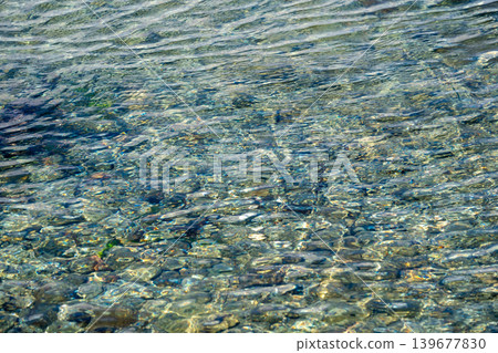 Clear turquoise waters ripple over smooth pebbles in sunlit natural setting 139677830