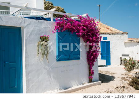Charming white mediterranean house with vibrant bougainvillea and blue accents on a sunny day Charming white mediterranean house with vibrant bougainvillea and blue accents on a sunny day 139677945