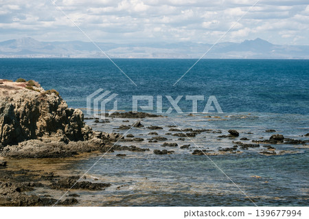 Rocky coastal landscape with tranquil waters under cloudy sky Rocky coastal landscape with tranquil waters under cloudy sky 139677994