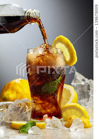 Cola is poured from a bottle into a misted glass with lemon slices, ice and mint. 139678009
