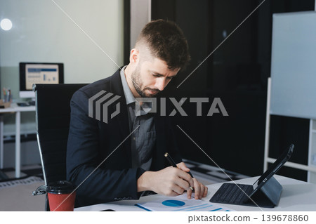 Tired worker. A tired businessman works in the evening. A man in office clothes is holding his temples. Problems in business. The businessman is trying to solve the problems that have arisen. 139678860