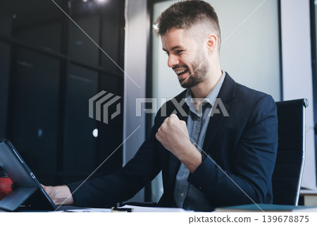 Smiling businessman in suit works on laptop in bright modern office Smiling businessman in suit works on laptop in bright modern office 139678875