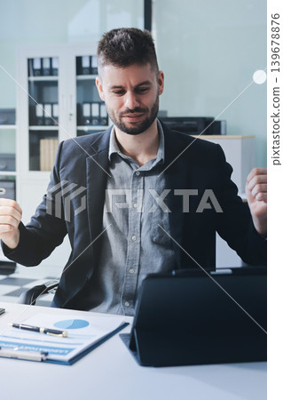 Smiling businessman in suit works on laptop in bright modern office Smiling businessman in suit works on laptop in bright modern office 139678876