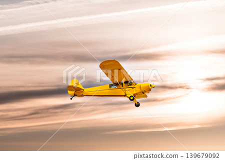 A yellow single-engine ultralight flying under an orange sky at sunset. A yellow single-engine ultralight flying under an orange sky at sunset. 139679092