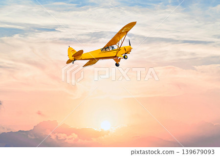 A yellow single-engine ultralight flying under an orange sky at sunset. A yellow single-engine ultralight flying under an orange sky at sunset. 139679093