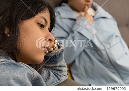 A teenager is sitting on a couch with her head down A teenager is sitting on a couch with her head down 139679903