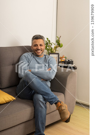 A man is sitting on a couch with his arms crossed 139679909