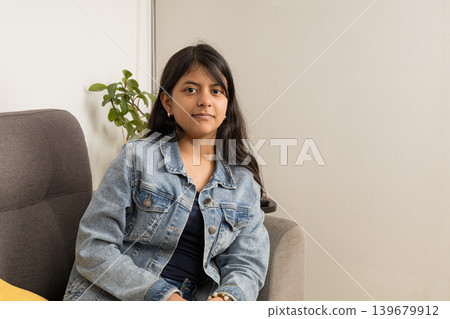 A teenager is sitting on a couch wearing a blue jacket 139679912