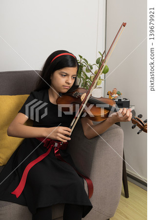 A young girl is playing the violin in a living room A young girl is playing the violin in a living room 139679921