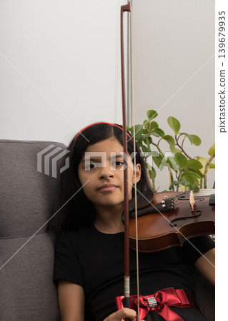 A young girl is sitting on a couch holding a violin A young girl is sitting on a couch holding a violin 139679935