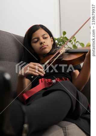 A young girl is playing the violin in a living room A young girl is playing the violin in a living room 139679937