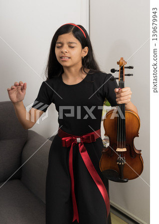 A young girl in a black dress is holding a violin 139679943