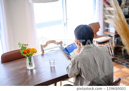 一名男子背對著鏡頭，坐在桌旁看書。 139680001