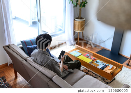 一名男子坐在沙發上,看著他的智慧型手機,鏡頭從他的背影拍攝。 一名男子坐在沙發上,看著他的智慧型手機,鏡頭從他的背影拍攝。 139680005