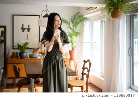 A woman in a green dress standing by the window. A woman in a green dress standing by the window. 139680017