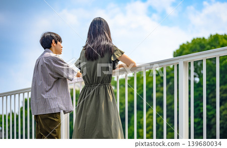 Two people gazing at the greenery from behind a railing under a blue sky. Two people gazing at the greenery from behind a railing under a blue sky. 139680034