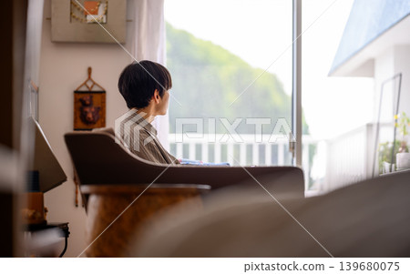一個男人背對著鏡頭，凝視著窗外的綠色植物。 139680075