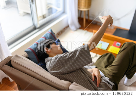 A man is lying on a sofa, holding his smartphone. A man is lying on a sofa, holding his smartphone. 139680122