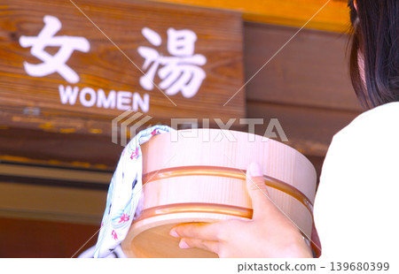 A sign for the women's bath at the entrance of the hot spring resort, and a woman holding a bath bucket. A sign for the women's bath at the entrance of the hot spring resort, and a woman holding a bath bucket. 139680399