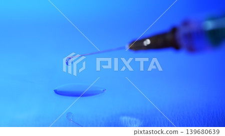 Needle approaches droplet in blue background during science experiment on fluid dynamics Needle approaches droplet in blue background during science experiment on fluid dynamics 139680639