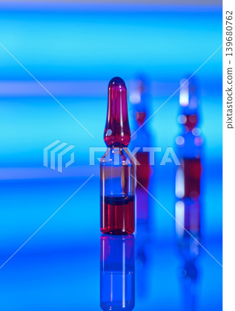 Colorful glass ampoules stand on a reflective surface with a blue background in a modern setting during daytime Colorful glass ampoules stand on a reflective surface with a blue background in a modern setting during daytime 139680762