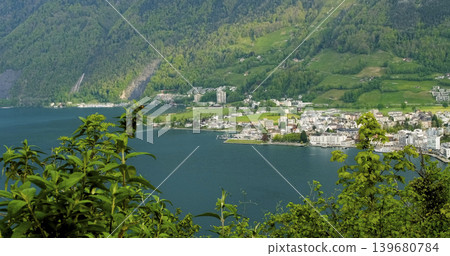 View of a lakeside town in Switzerland surrounded by green mountains during daytime View of a lakeside town in Switzerland surrounded by green mountains during daytime 139680784