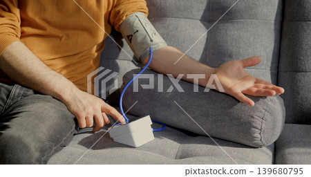 Man checks blood pressure at home while sitting on a gray couch 139680795