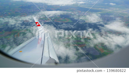 Plane wing viewed from window during flight over fields and clouds near airport in Switzerland 139680822