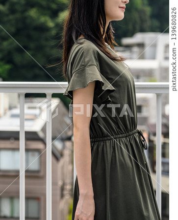 一位身穿洋裝的女子側身站在綠色背景前。 139680826