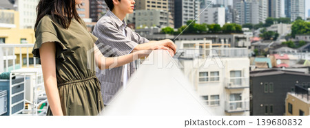 A man and a woman leaning against the railing on the rooftop. A man and a woman leaning against the railing on the rooftop. 139680832