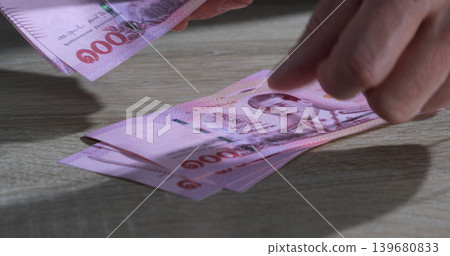 Counting Thai banknotes on a wooden table in a well-lit room during the day Counting Thai banknotes on a wooden table in a well-lit room during the day 139680833