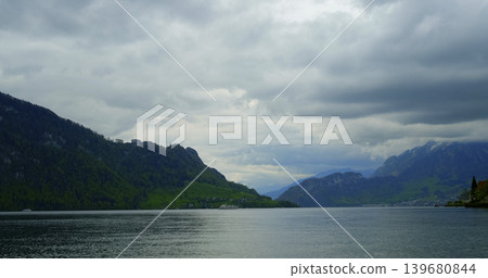 View of mountains and lake under cloudy sky in Switzerland during daytime with boats in the distance View of mountains and lake under cloudy sky in Switzerland during daytime with boats in the distance 139680844