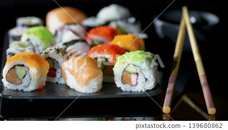 Many types of sushi arranged on a black plate with chopsticks and a small bowl in the background Many types of sushi arranged on a black plate with chopsticks and a small bowl in the background 139680862