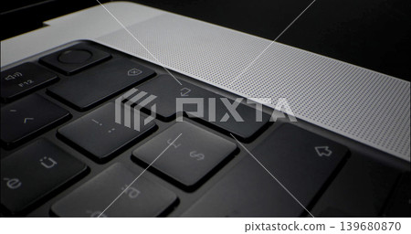 Close view of a laptop keyboard showing keys, speakers, and design details on a black surface during a work session Close view of a laptop keyboard showing keys, speakers, and design details on a black surface during a work session 139680870